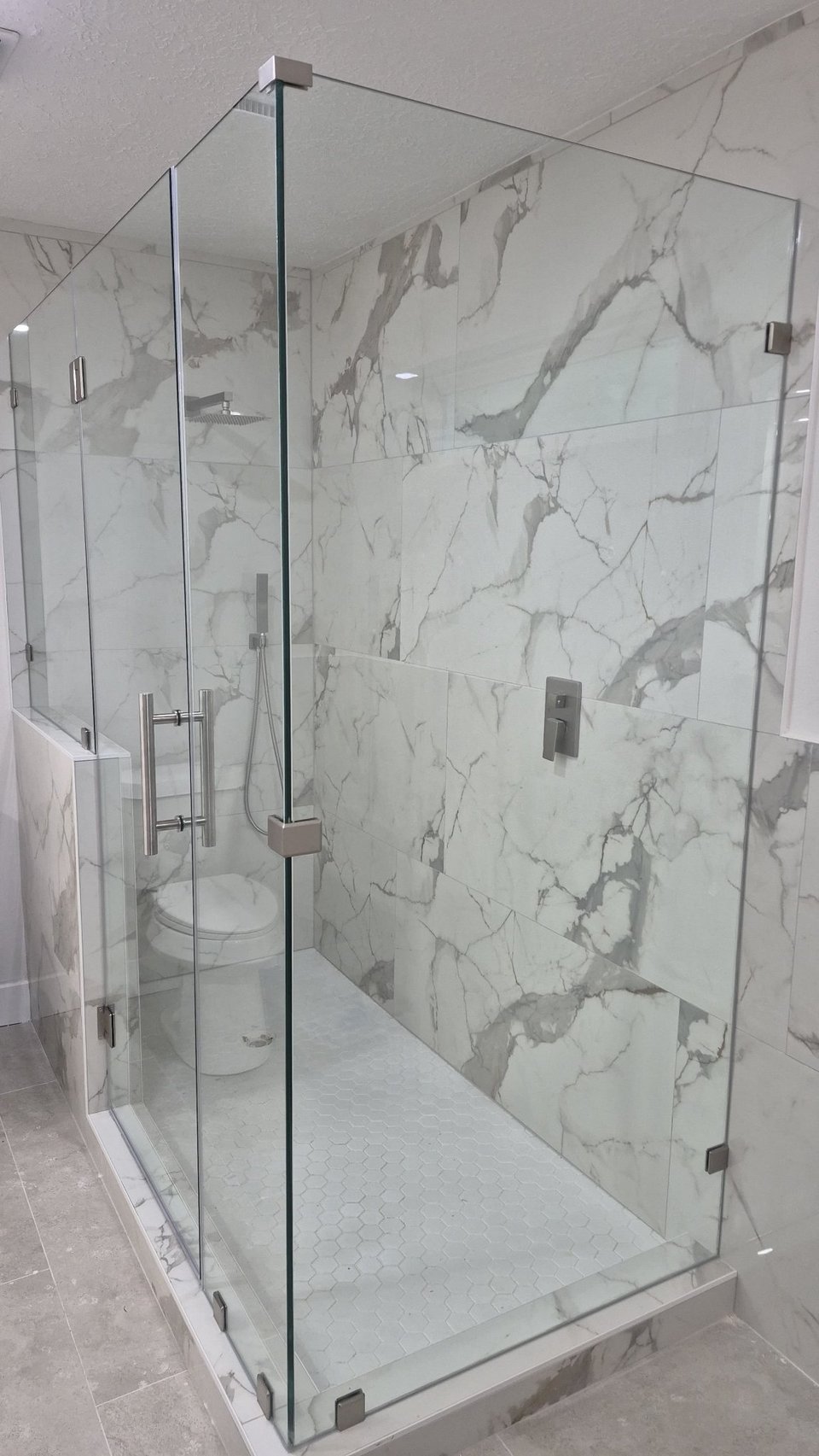Ejemplo de ángulo 90° sobre muros / muretes de Glas Plus: vidrio clear con herraje de níquel en un baño de mármol, con un panel montado sobre un murete