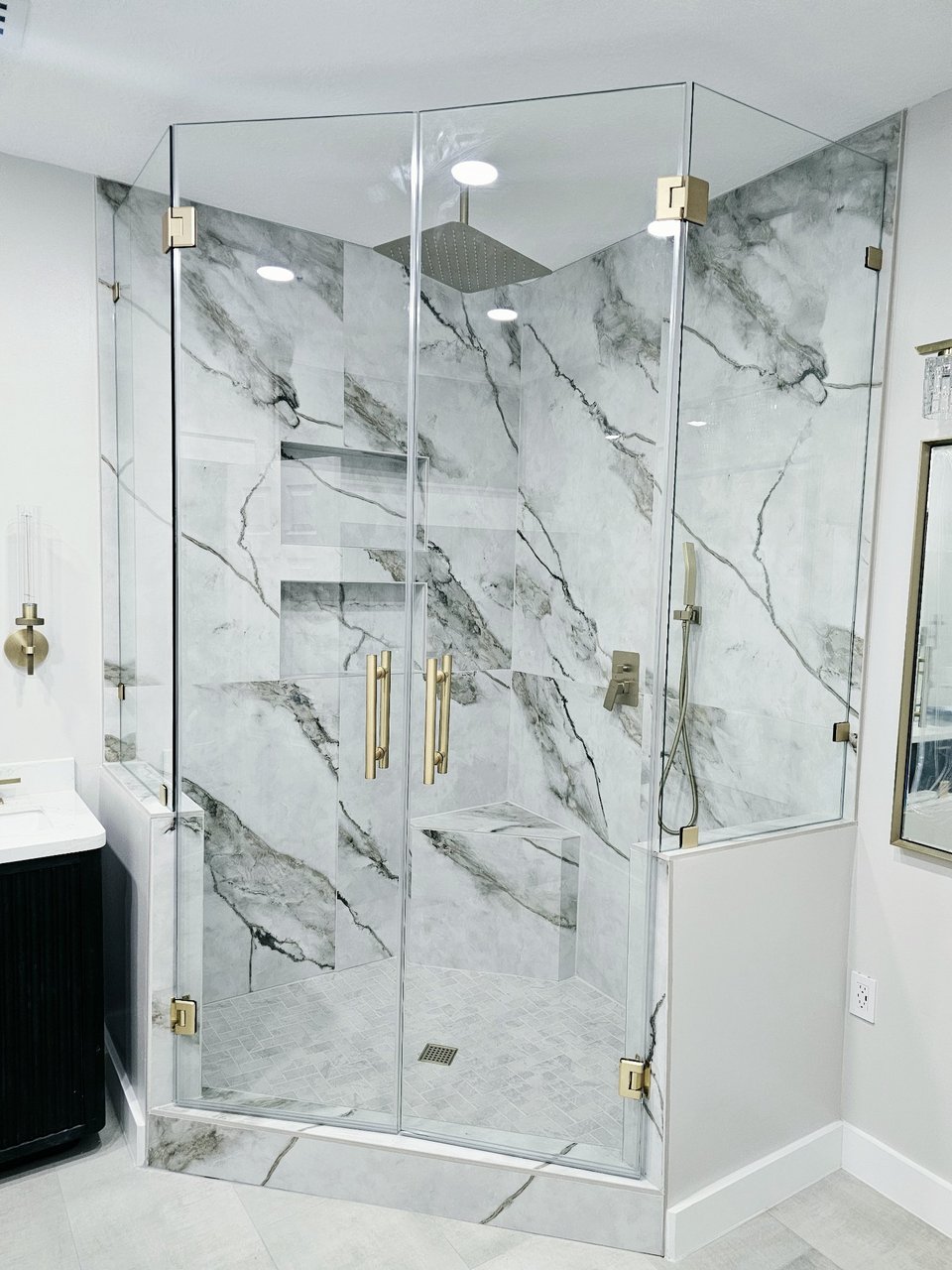 Ejemplo de ángulo 90° sobre muros / muretes de Glas Plus: vidrio clear con herraje brush gold montado sobre medios muros, en un baño de mármol