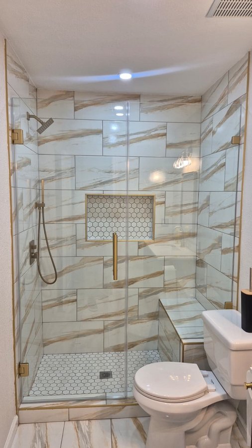 Ejemplo de bisagras con muro de Glas Plus: puerta de bisagras a la pared y panel fijo junto a la banca de azulejo del shower, con herraje brush gold