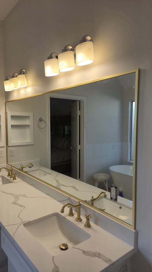 Ejemplo de espejos de Glas Plus: espejo grande de tocador con frame de metal dorado sobre un tocador doble de mármol