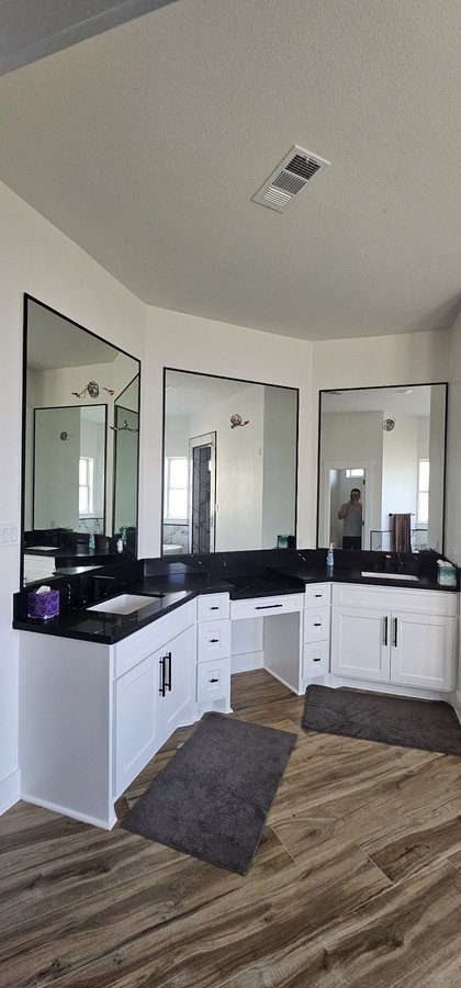 Ejemplo de espejos de Glas Plus: tres espejos con frame de metal negro en un baño con tocadores blancos