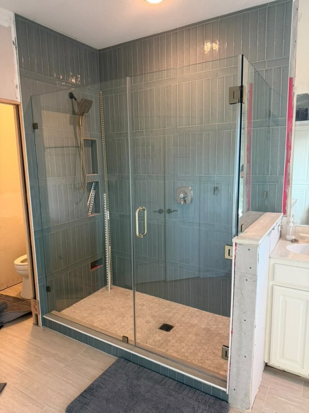 Trabajo de Glas Plus: ángulo 90° con herraje de níquel junto a un medio muro, en un shower de azulejo azul grisáceo