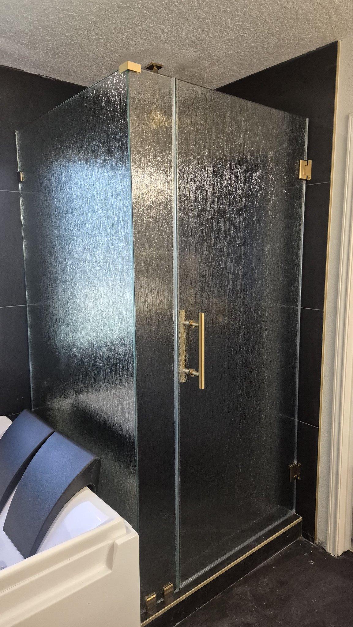 Trabajo de Glas Plus: shower en ángulo 90° con vidrio Rain (textura de lluvia) y herraje dorado