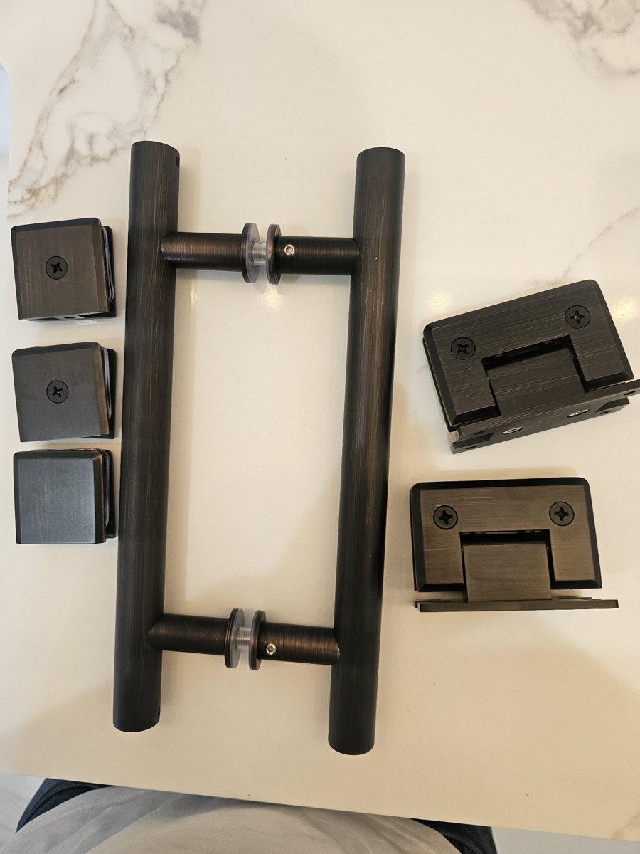 Juego completo de herraje en bronce oscuro de Glas Plus: manijas, clips y bisagras sobre una mesa de mármol