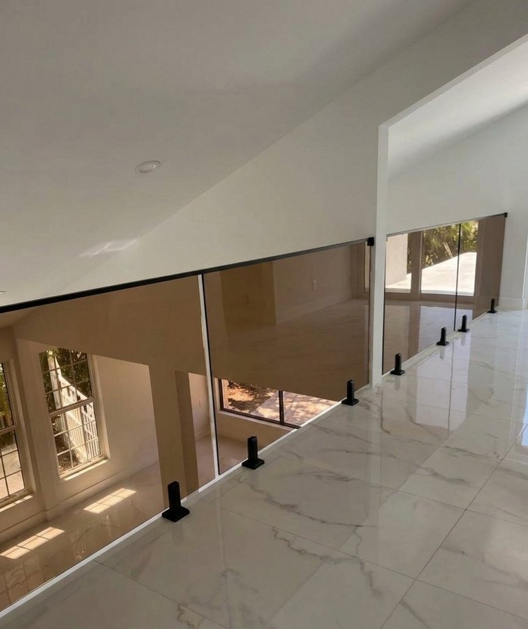 Ejemplo de balcones de Glas Plus: barandal de vidrio ahumado en un balcón interior de doble altura, con piso de mármol