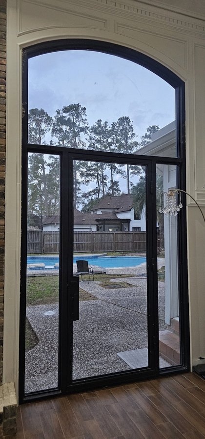 Ejemplo de storefront de Glas Plus: puerta de vidrio con arco superior y marco negro, vista hacia el patio y la piscina