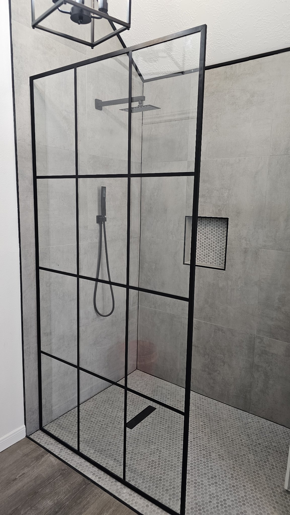 Foto de referencia del panel con rejillas estilo industrial de Glas Plus: panel fijo de vidrio clear con rejilla metálica negra en un shower abierto