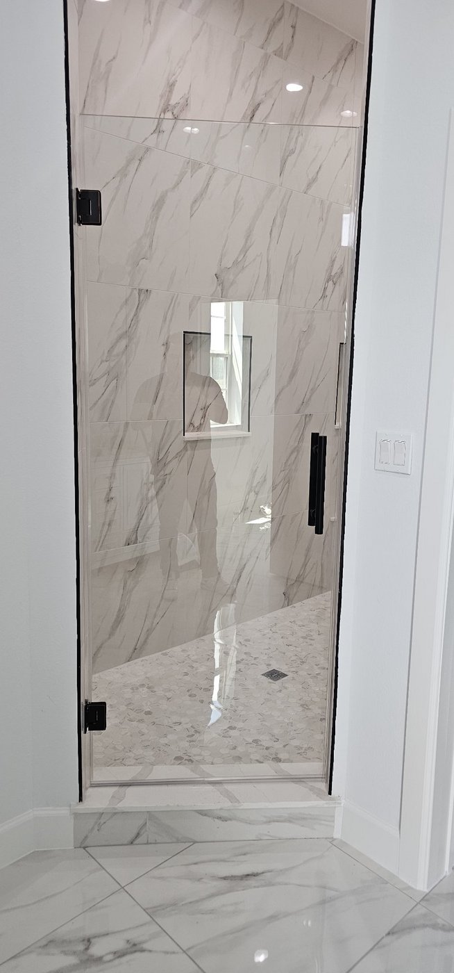 Single door con herraje negro instalada por Glas Plus en un baño de mármol blanco
