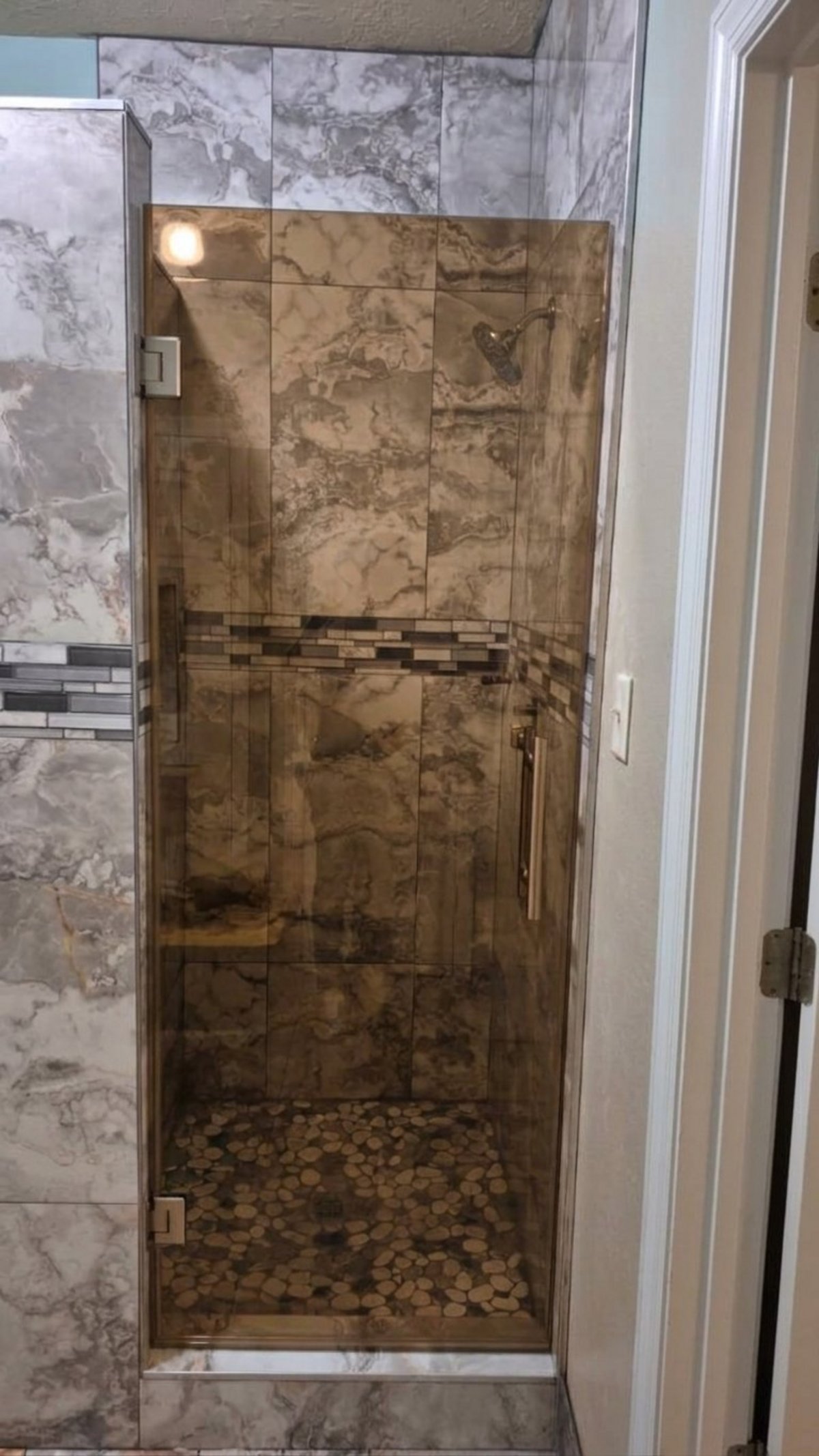 Single door con vidrio Bronze (tono bronce) y herraje brush nickel instalada por Glas Plus en un shower de azulejo tipo mármol
