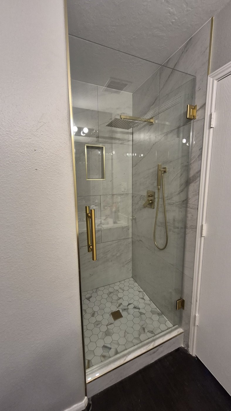 Single door con herraje brush gold instalada por Glas Plus en un shower de mármol con ducha de lluvia