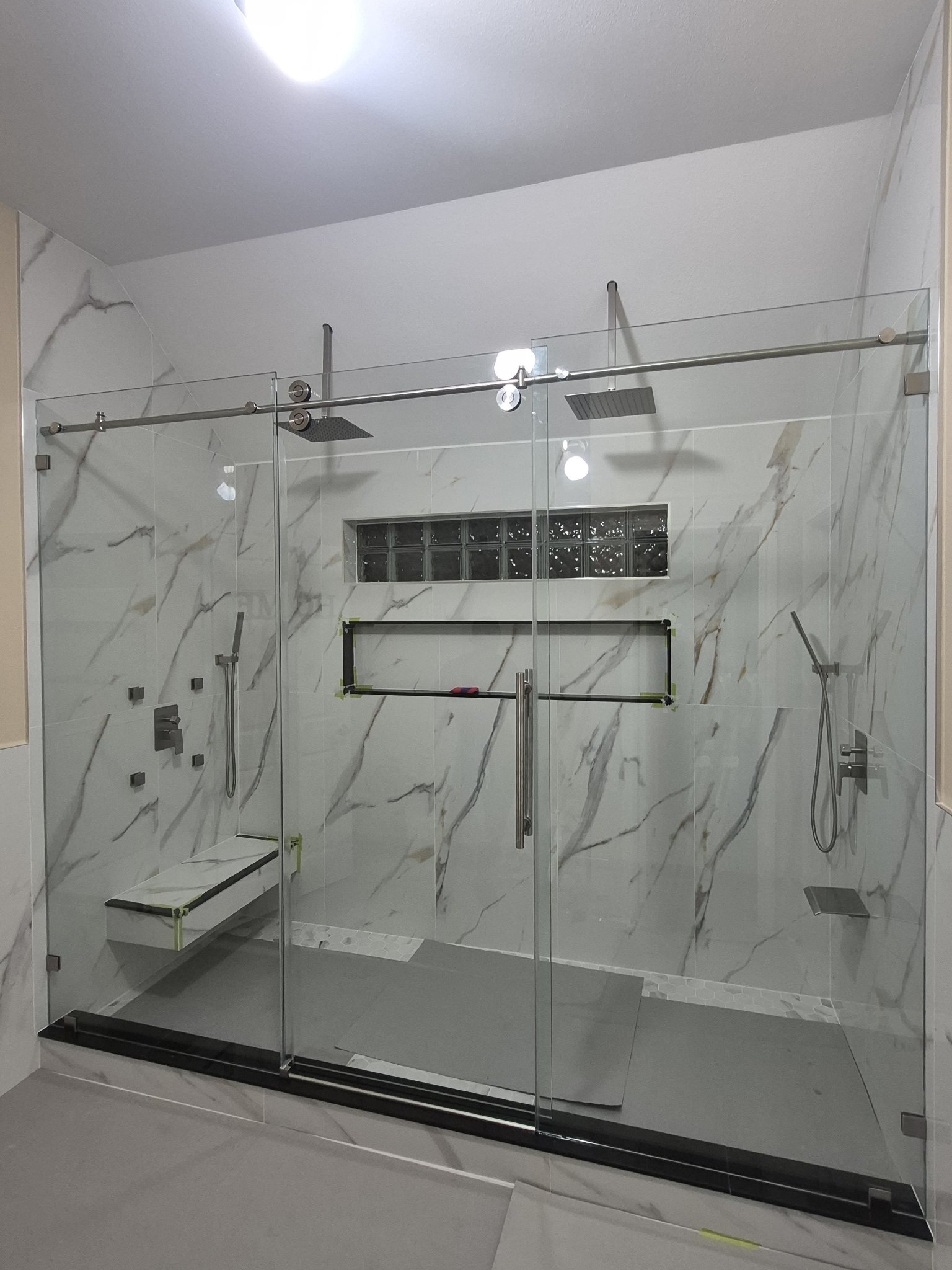 Sliding con puerta en el centro (panel fijo, puerta y panel fijo) con riel de brush nickel en shower amplio de mármol con dos duchas y banca