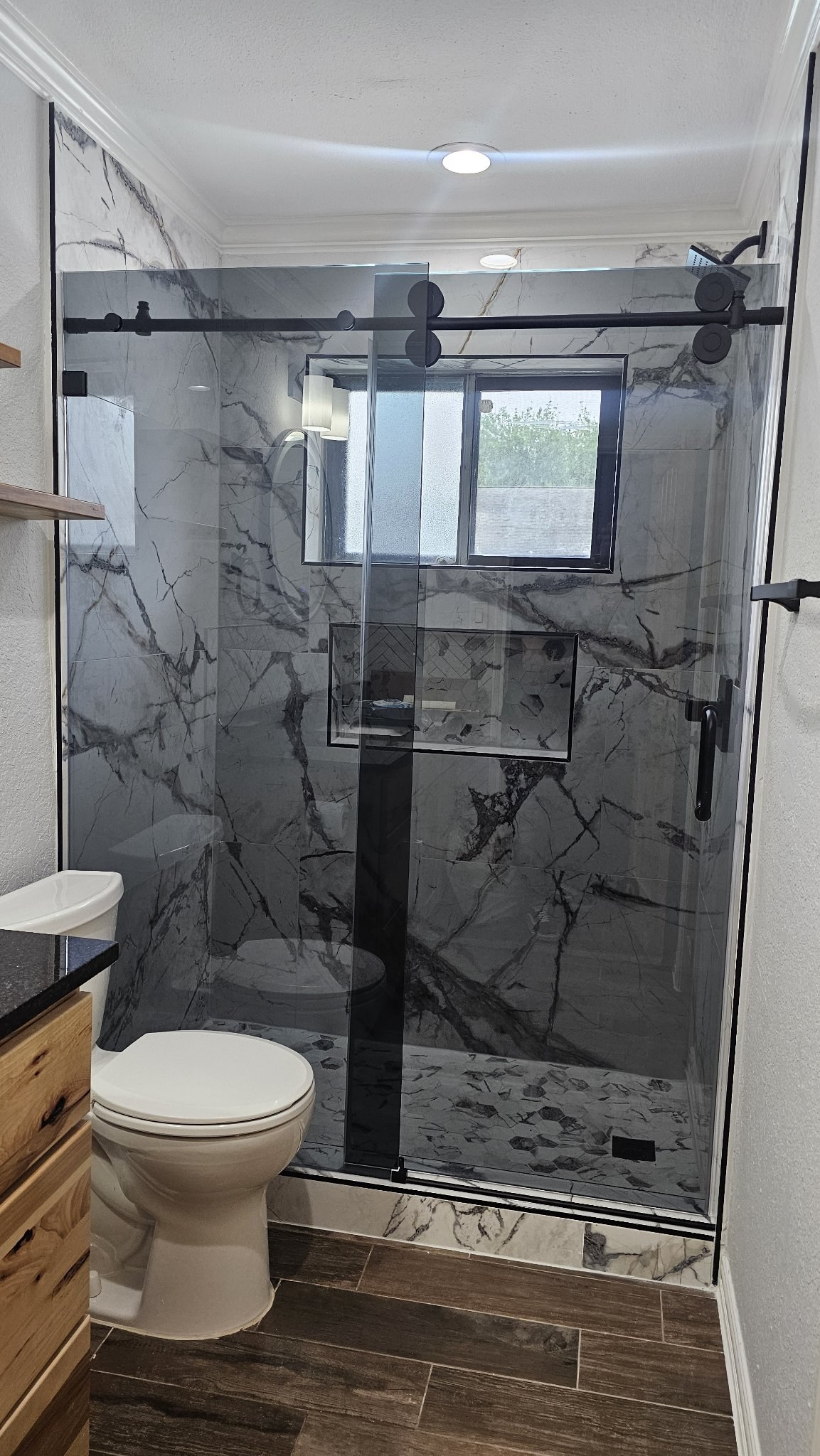 Sliding de una puerta con vidrio Grey (gris ahumado), barra negra y panel fijo en shower de mármol veteado con nicho