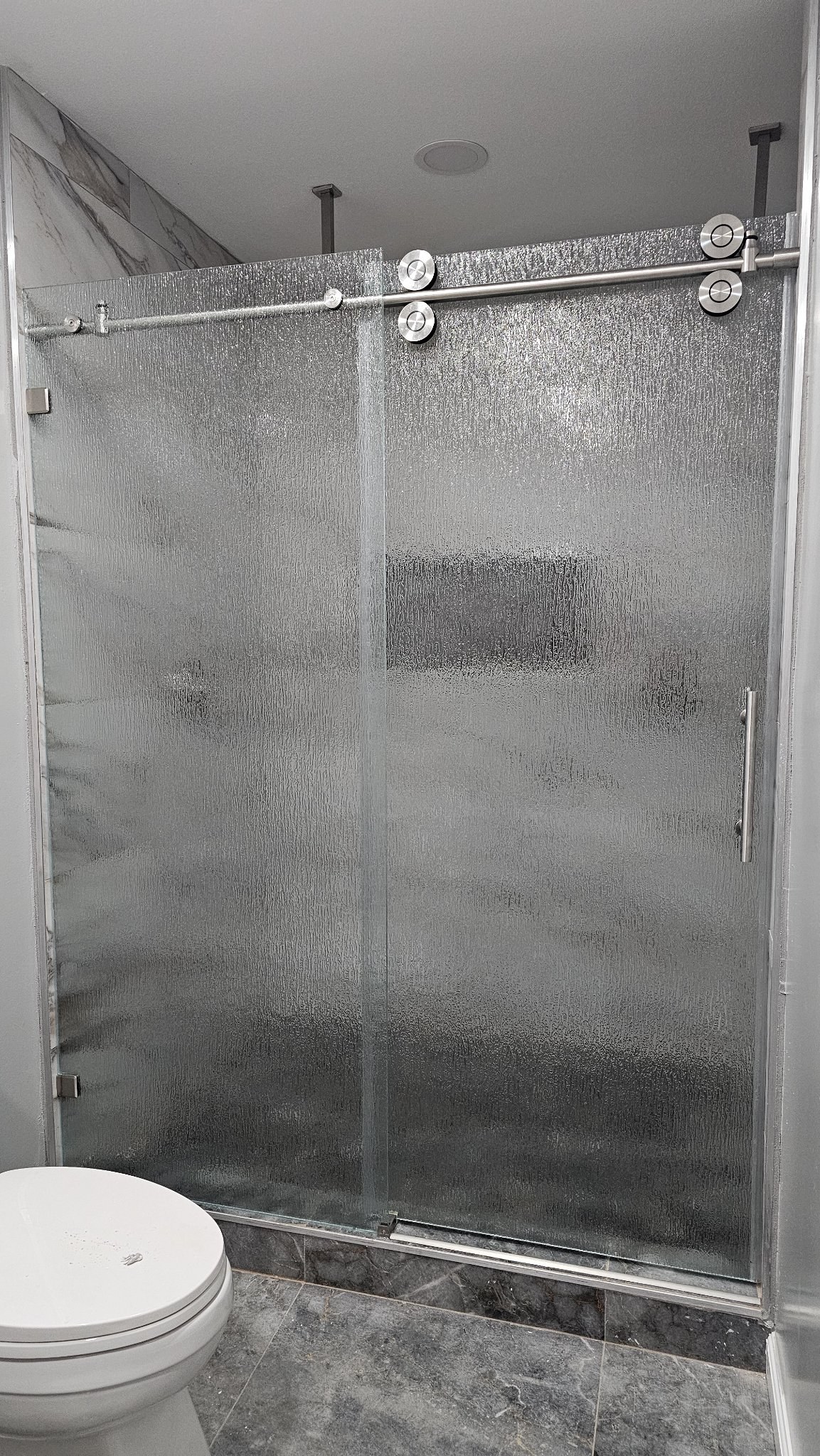 Sliding de una puerta con vidrio Rain (textura de lluvia), riel de níquel cepillado y panel fijo en shower de azulejo mármol
