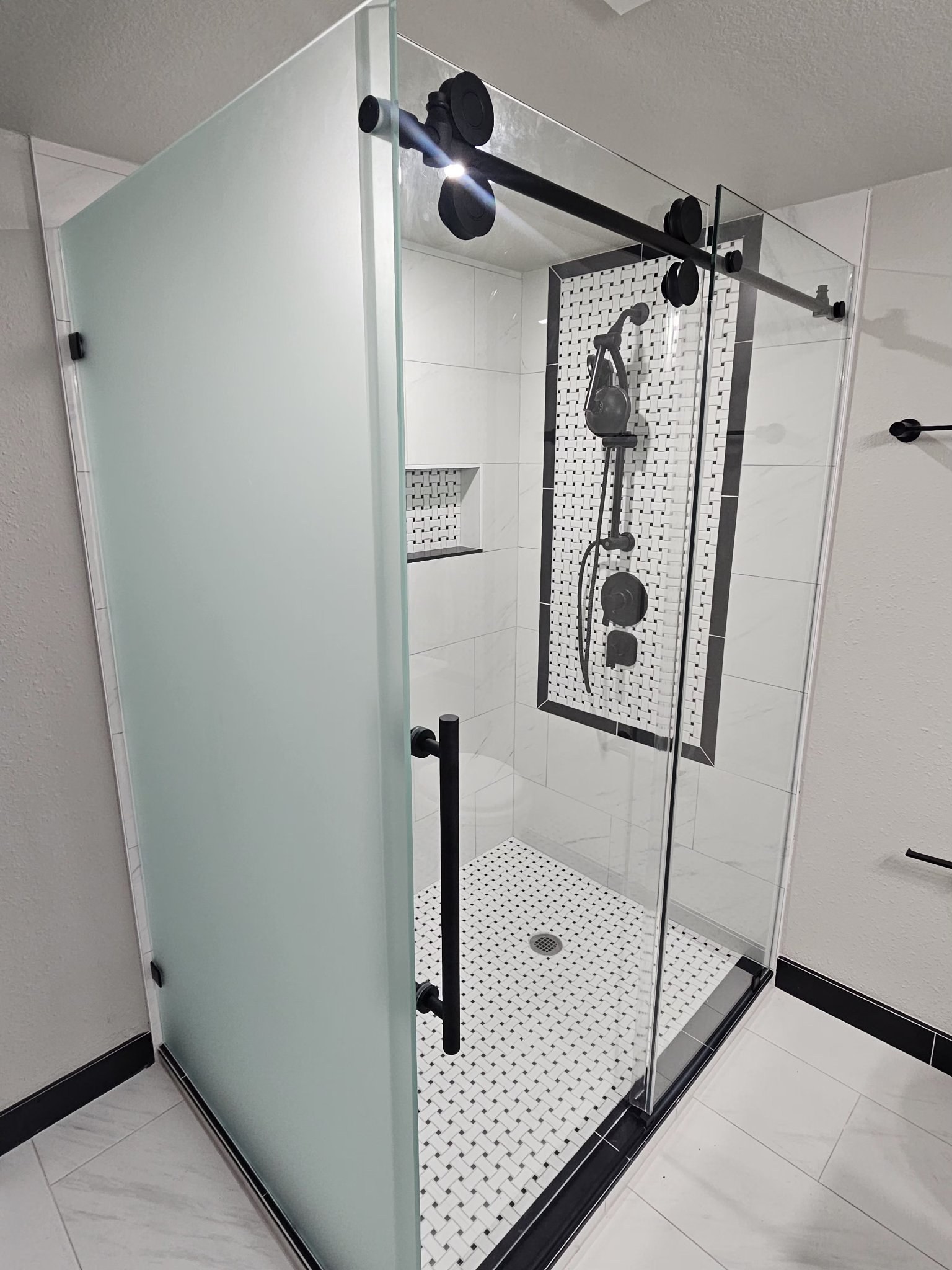 Sliding con retorno de vidrio Frosted (opaco) y barra negra en shower de azulejo blanco con mosaico