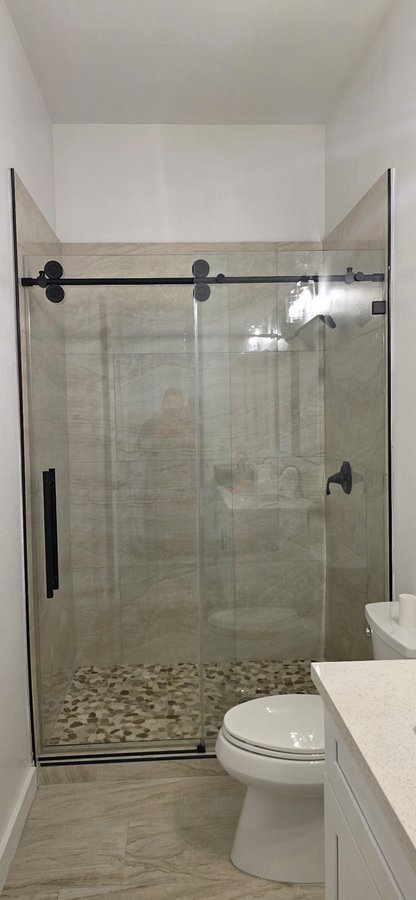 Sliding de una puerta con riel negro y panel fijo en shower de azulejo blanco