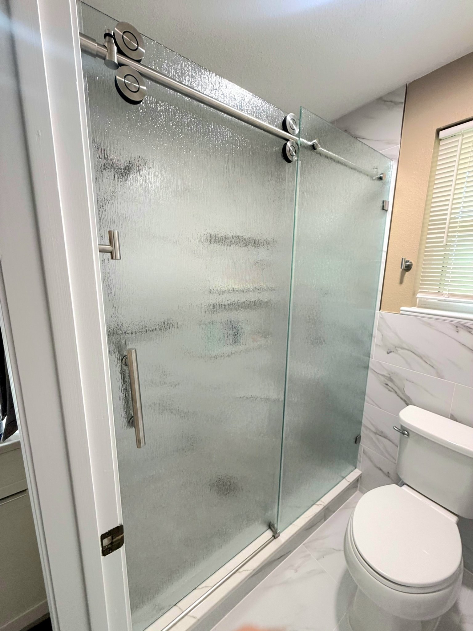 Sliding de una puerta con vidrio Rain (textura de lluvia), riel de níquel cepillado y panel fijo en shower de azulejo mármol